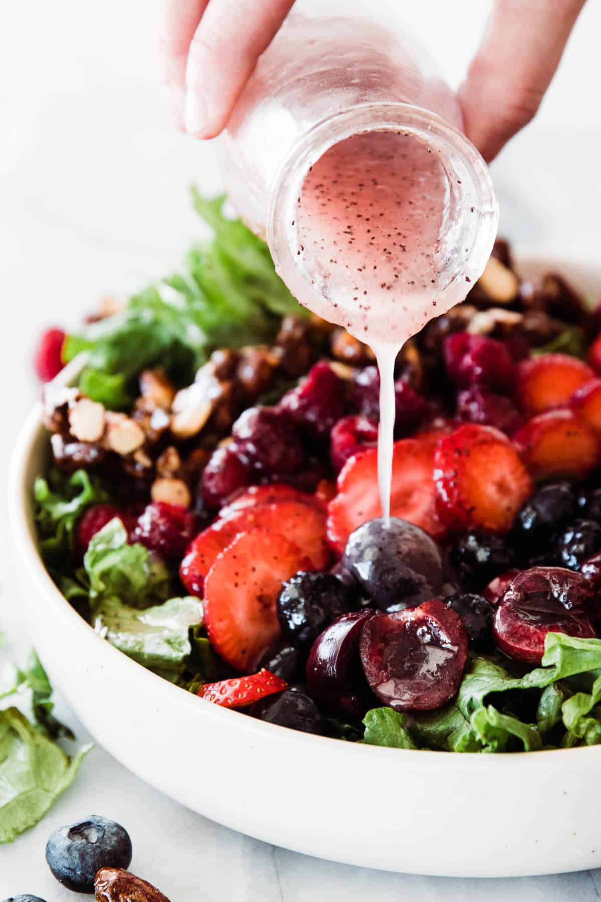 Pink Poppyseed dressing drizzling over berry salad.