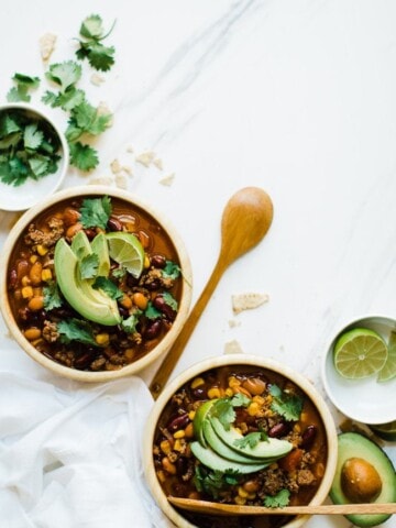 Easy pressure cooker taco soup in wooden bowls with wooden spoon, topped with avocado and cilantro.