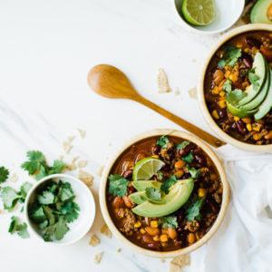 Easy pressure cooker taco soup in wooden bowls with wooden spoon, topped with avocado and cilantro.