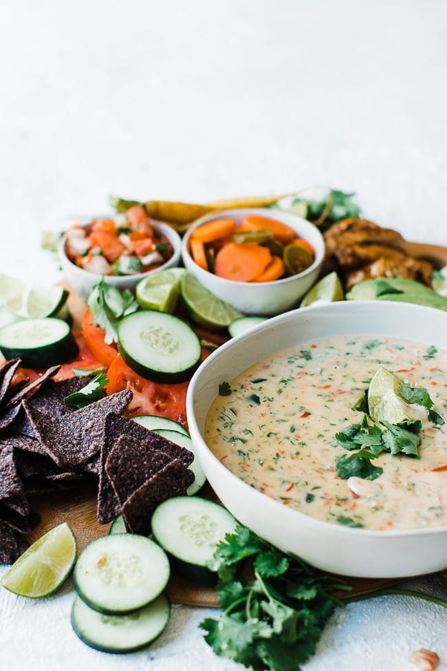 Queso Blanco Mexican White Cheese Dip on a wooden cutting board with chips, veggies, and chicken.