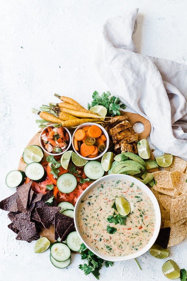 Queso Blanco Mexican White Cheese Dip on a wooden cutting board with chips, veggies, and chicken.