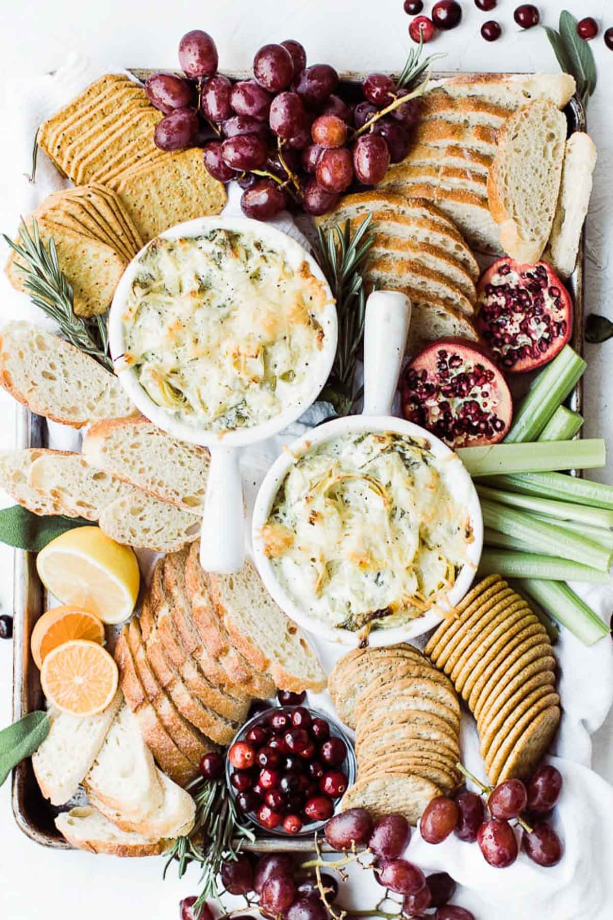 Two bowls of spinach artichoke dip with bread, crackers around them.