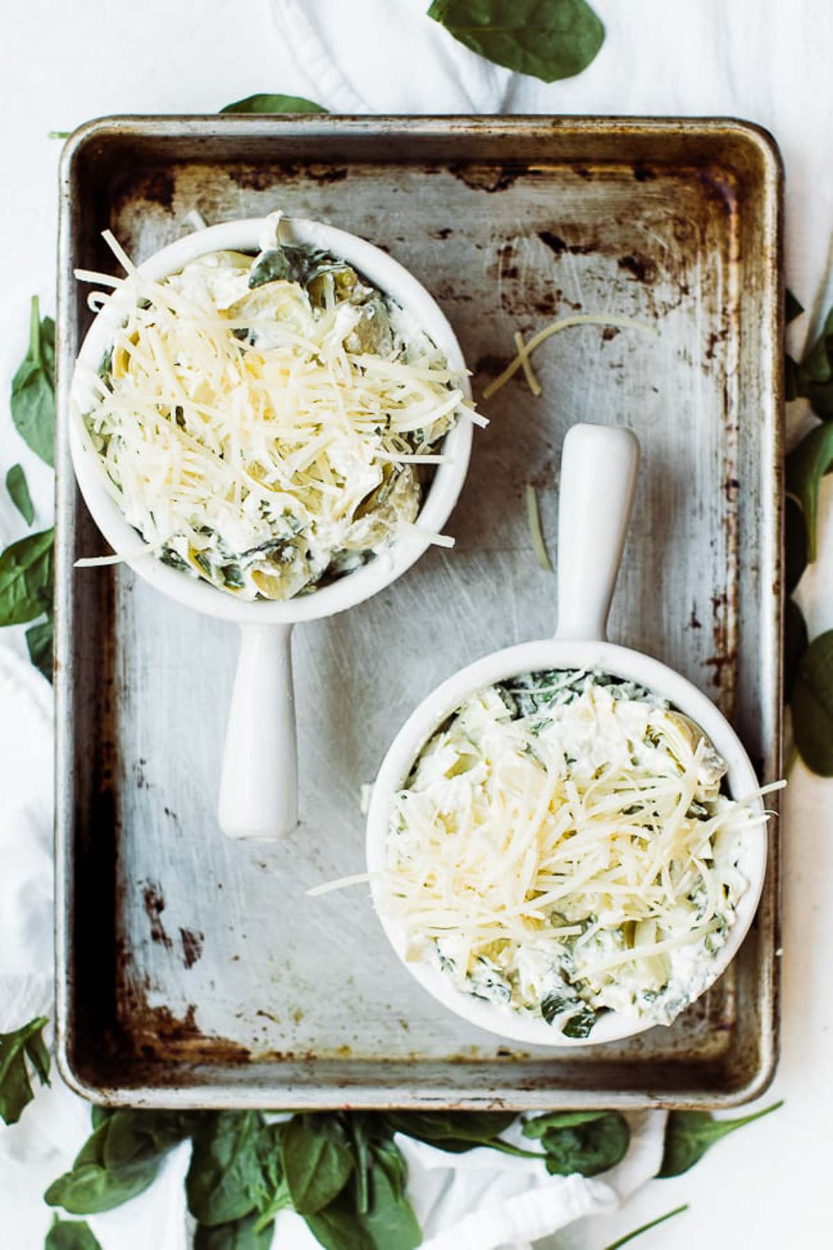 Two bowls of spinach artichoke dip with cheese on top