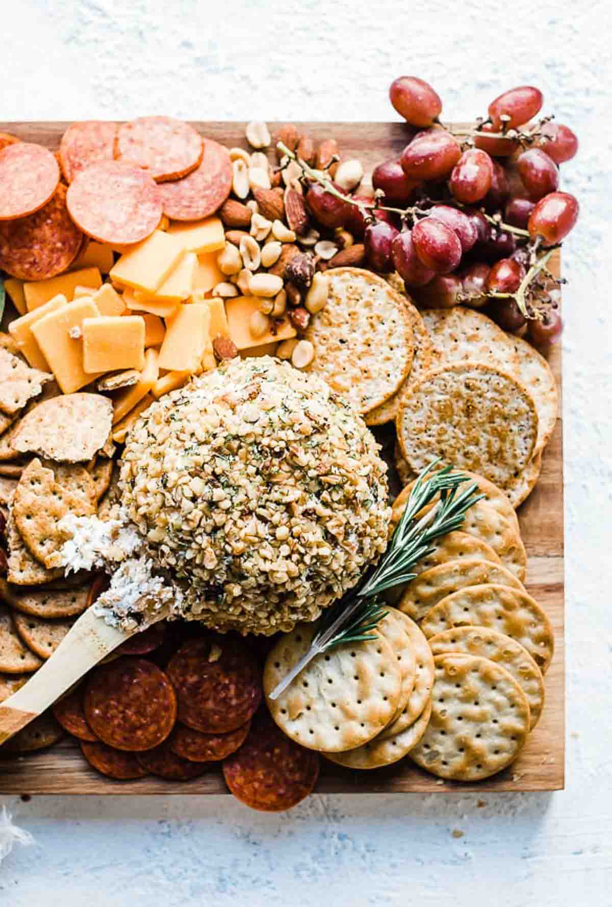 Ranch cheeseball recipe on a wooden cutting board with crackers, nuts, olives, grapes, and meats.