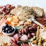 Ranch cheese ball recipe on a wooden cutting board with crackers, nuts, olives, grapes, and meats.