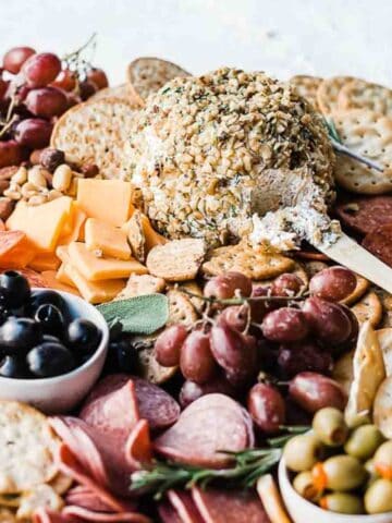 Ranch cheese ball recipe on a wooden cutting board with crackers, nuts, olives, grapes, and meats.