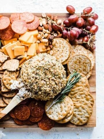 Ranch cheeseball recipe on a wooden cutting board with crackers, nuts, olives, grapes, and meats.