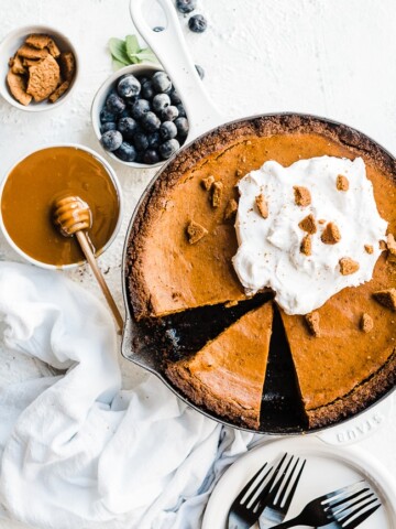Pumpkin pie with gingersnap crust in a cast iron pan with blueberries to the side.