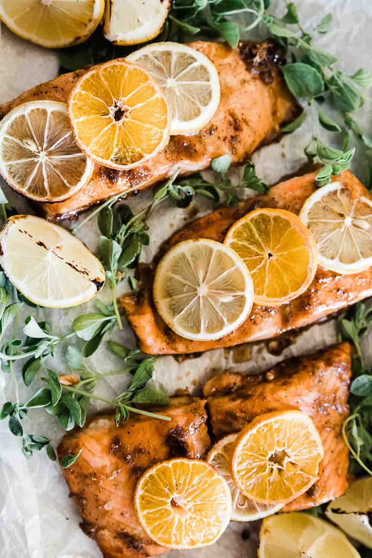 A closeup of orange glazed salmon on a baking tray, The salmon has citrus slices on top of it.