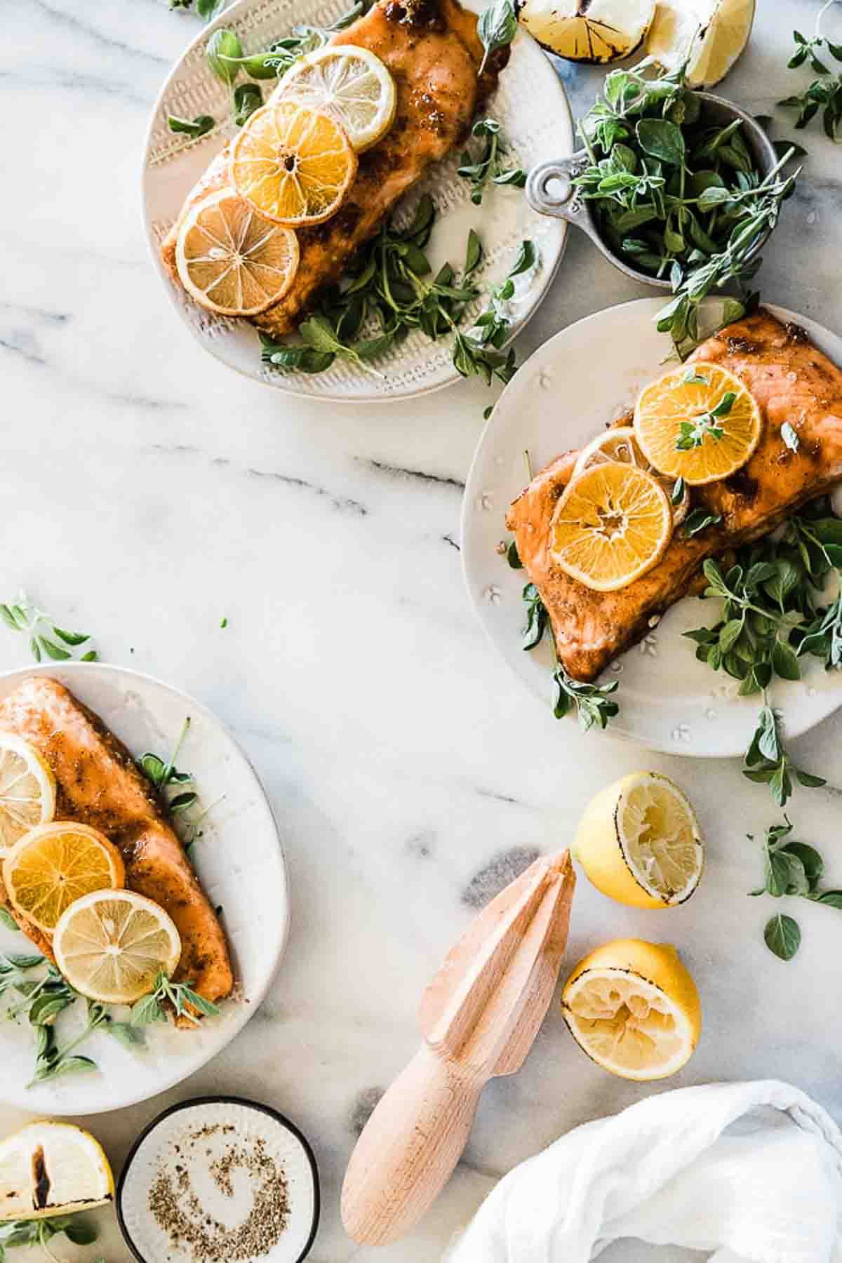 Glazed salmon on white plates, garnished with lemon slices and thyme.