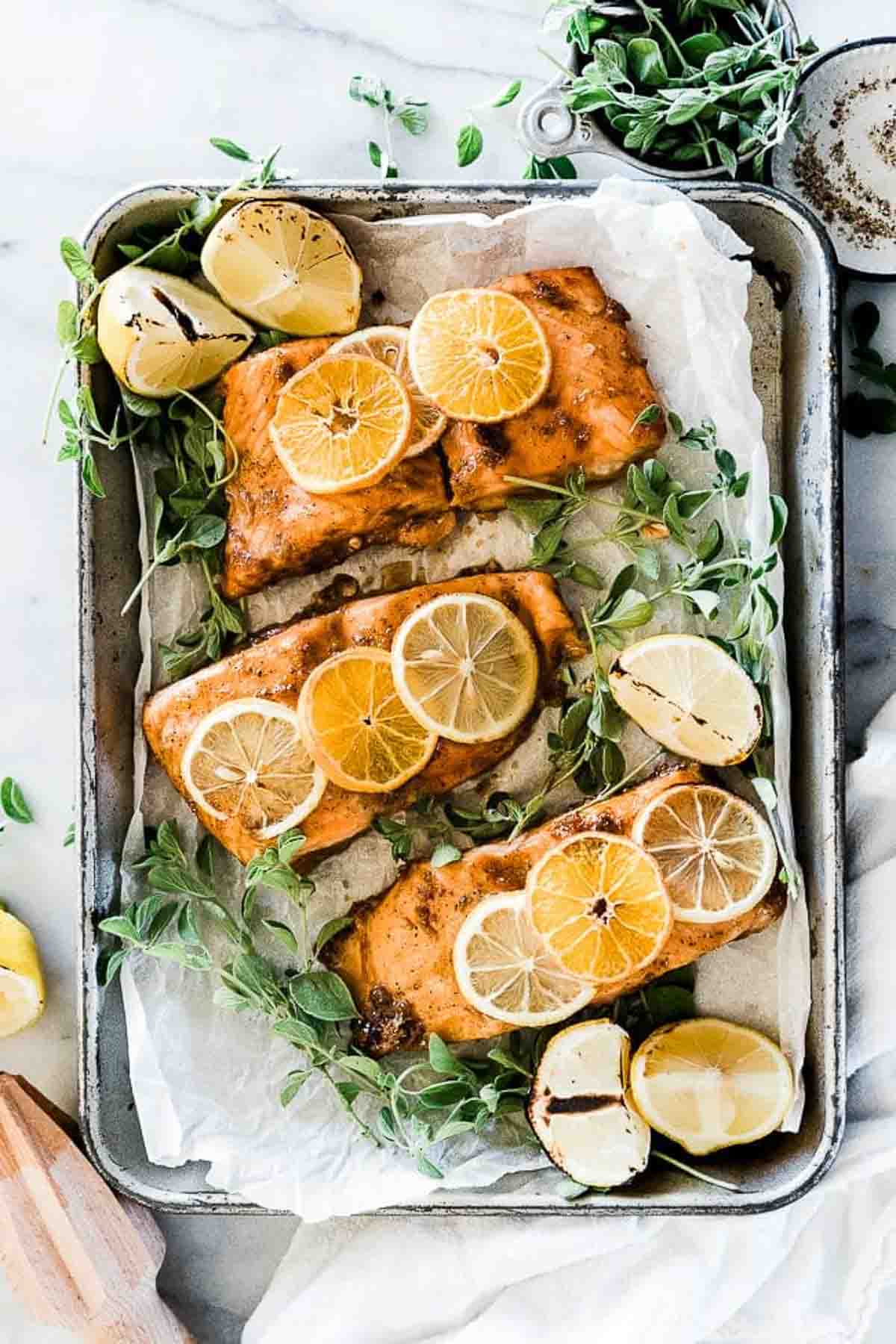Citrus salmon in a metal sheet pan, it is surrounded by greens and garnished with citrus slices.