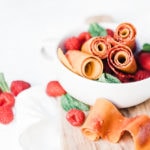Homemade peach and raspberry fruit leather in a white bowl with fresh raspberries.