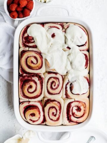 Raspberry sweet rolls being frosted with white chocolate icing.