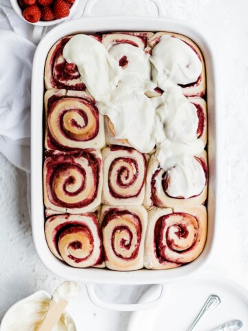 Raspberry sweet rolls being frosted with white chocolate icing.