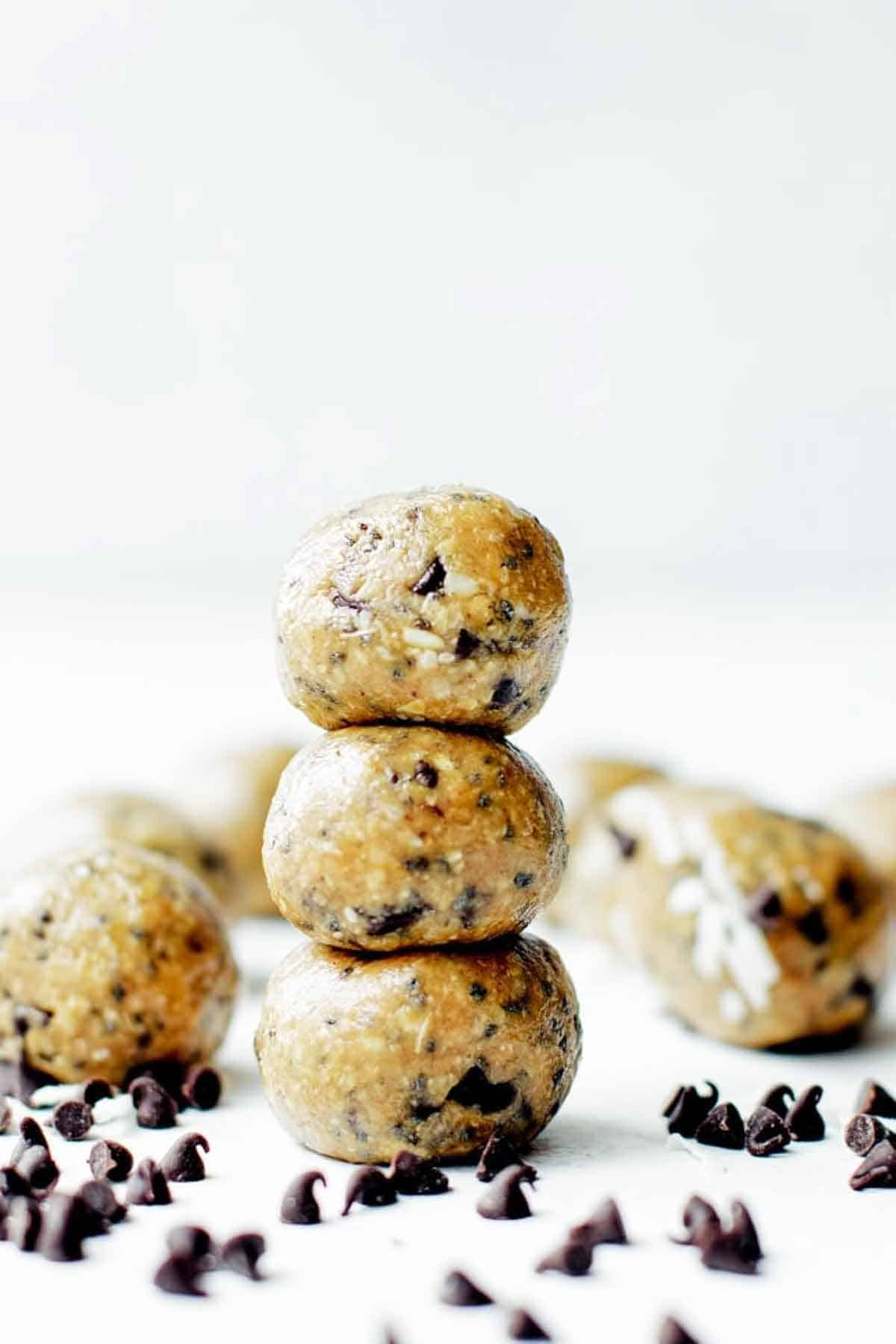 Three protein energy balls stacked on the table with chocolate chips scattered around them.