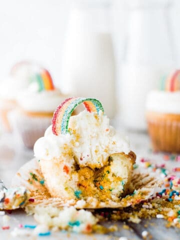 funfetti cupcake with white frosting and sour rainbow candy on top in rainbow shape, sprinkles falling out of the center