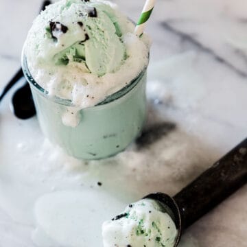 Shamrock soda float in a glass. There is a melting scoop of ice cream to the side.