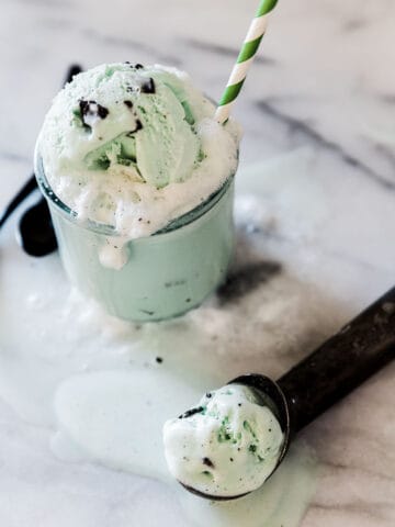 Shamrock soda float in a glass. There is a melting scoop of ice cream to the side.