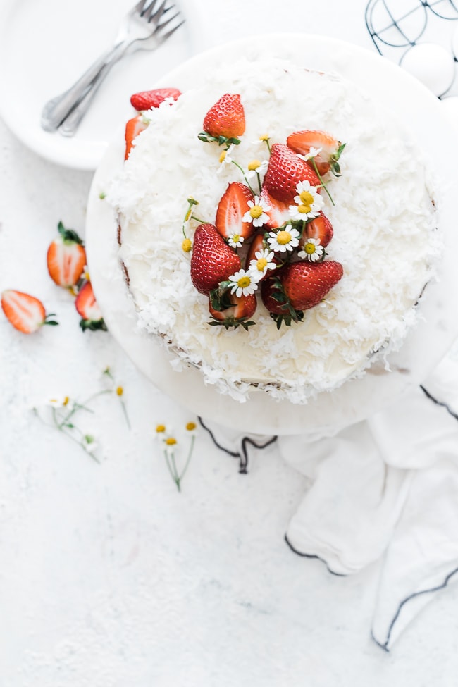 Coconut Strawberry Cake on a marble cake stand. Garnished with strawberries and white flowers.