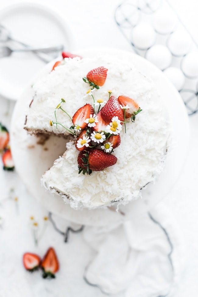 Coconut Strawberry Cake on a marble cake stand. Garnished with strawberries and white flowers.