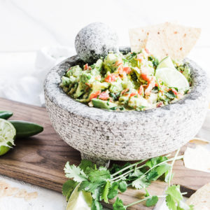 Healthy guacamole in a concrete bowl, atop a wooden cutting board.