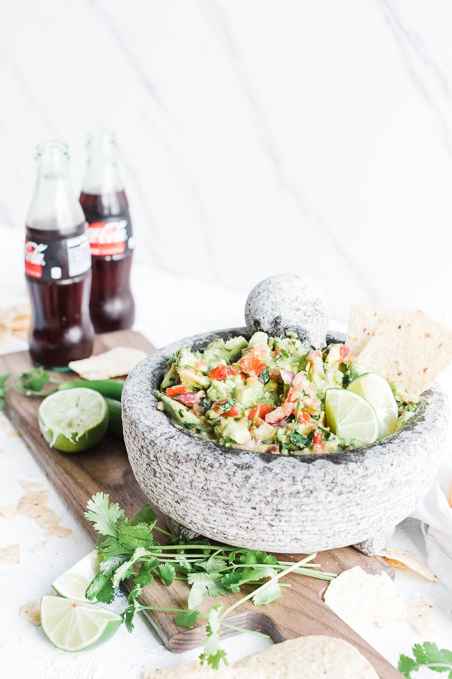 Healthy guacamole in a concrete bowl, atop a wooden cutting board.