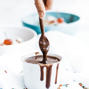 Homemade hot fudge being spooned from a white bowl.