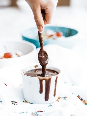 Homemade hot fudge being spooned from a white bowl.
