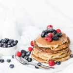 Healthy protein pancakes on a white plate - garnished with berries and powdered sugar.