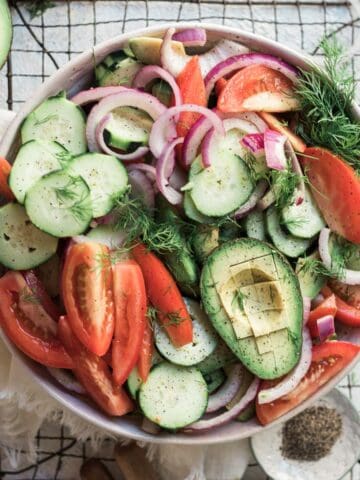 Cucumber tomato onion salad on the table on top of a wire rack with ingredients around the edges of the photo.