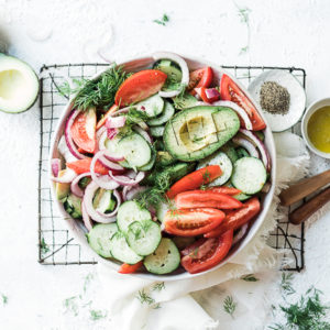Cucumber tomato red onion salad in white salad bowl. Atop a cooling rack, with dressing on the side.