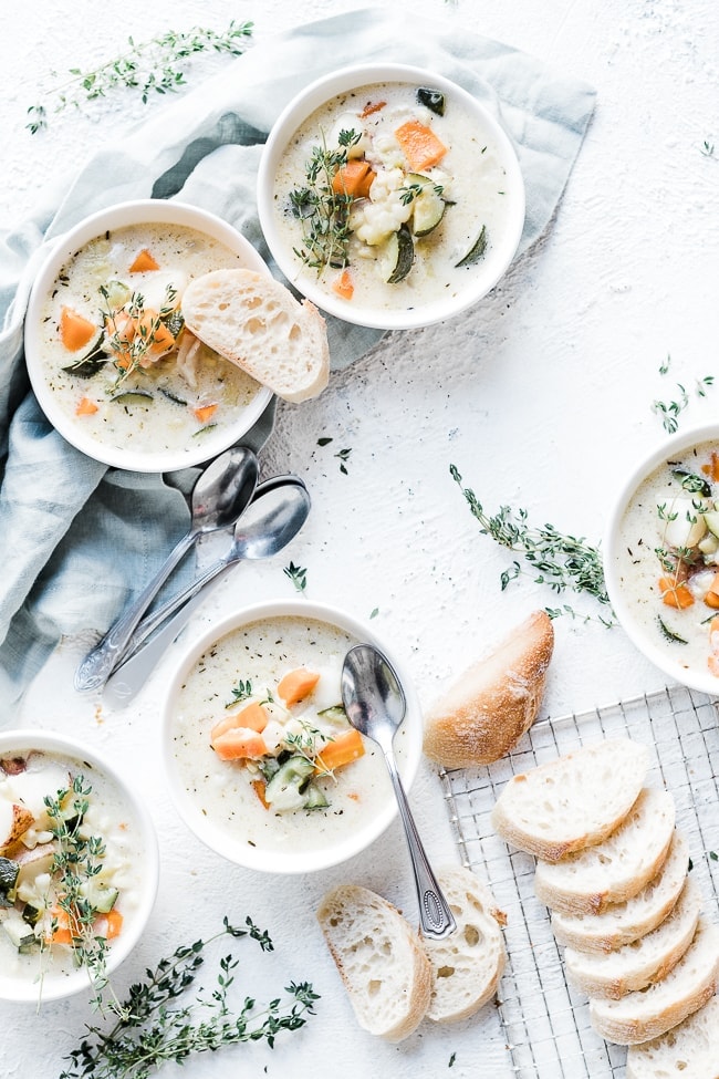 Summer corn chowder in white bowls, aside sliced bread, and garnished with thyme.