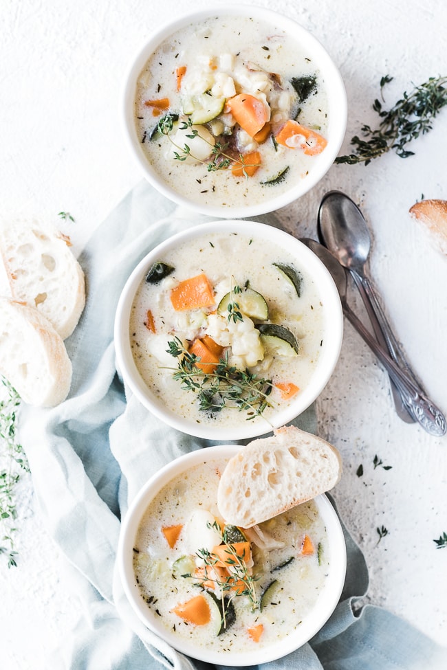 Summer corn chowder in white bowls, aside sliced bread, and garnished with thyme.
