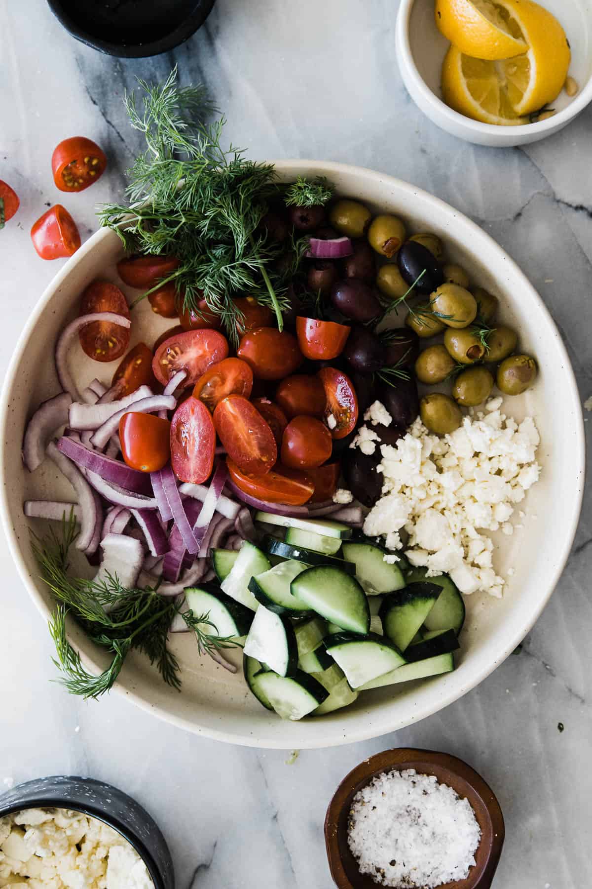 Olives, tomatoes, feta cheese, cucumbers, red onion and fresh dill in a large bowl for loaded greek hummus. 