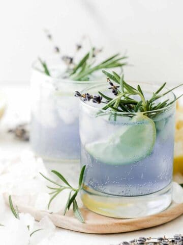 Sparkling lavender lemonade in glasses on a small board, surrounded by lemons and fresh lavender.