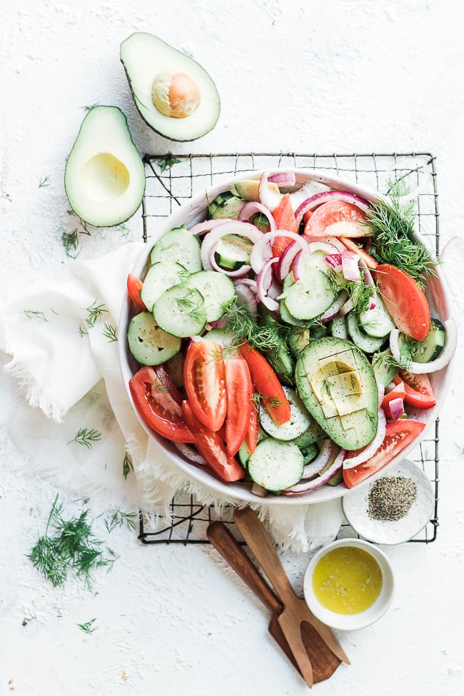 Cucumber tomato red onion salad in a white salad bowl, atop a cooling rack.