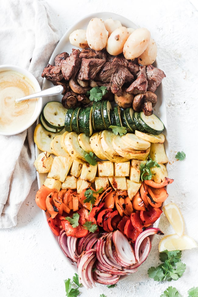 Grilled veggies and steak on a silver platter.