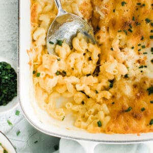 Casserole dish of creamy mac and cheese in casserole dish with spoon and portion missing.