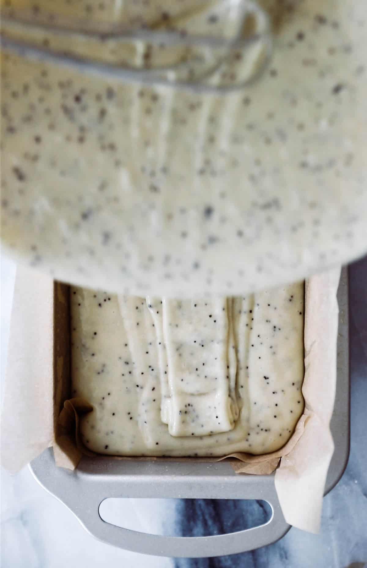 Pouring poppy seed loaf batter into a bread pan lined with parchment paper. 