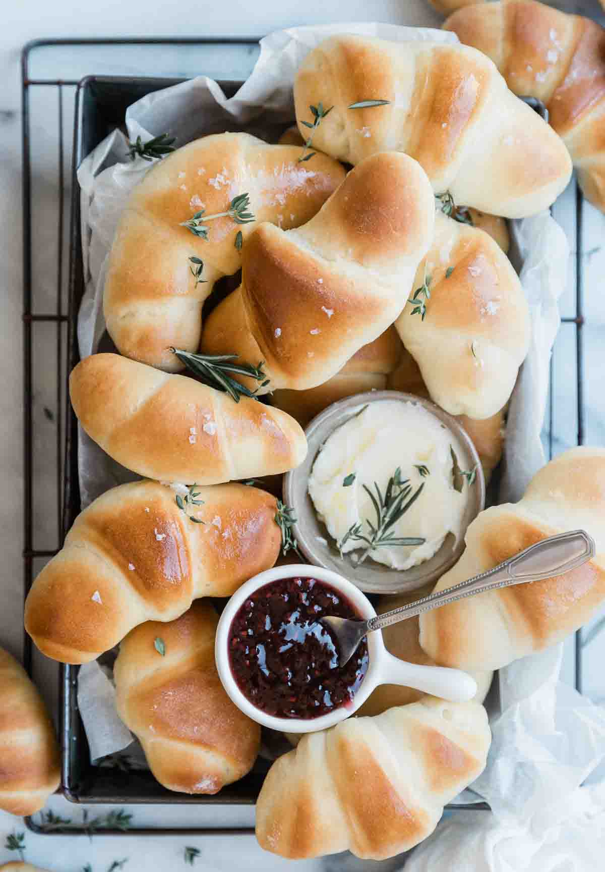 Easy crescent roll recipe rolls in a metal baking tray. There are small bowls of butter and jam nestled in the jam.