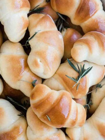 A close up of crescent rolls. They are brushed with butter and sprinkled with rosemary.