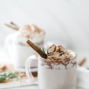 Pressure cooker warm milk and cinnamon in glass mugs, topped with whipped cream and garnished with rosemary and a cinnamon stick.