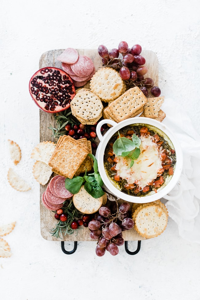 cream cheese pesto dip on a cheese board surrounded by crackers, grapes, and salami.