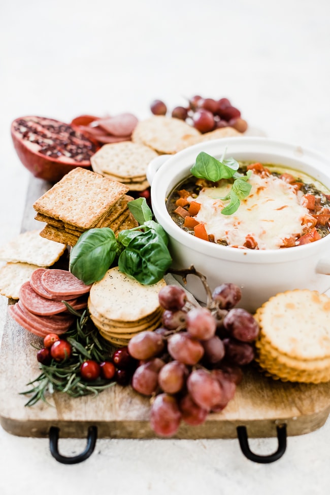 cream cheese pesto dip on a cheese board surrounded by crackers, grapes, and salami.
