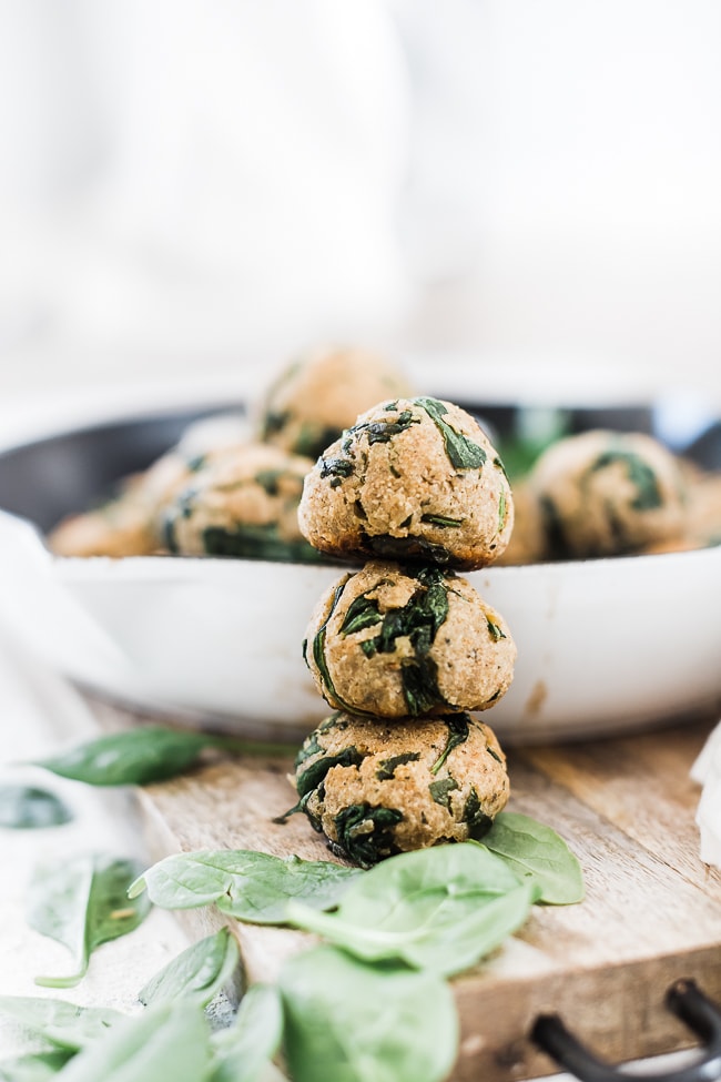 Spinach balls stacked beside a cast iron skillet.