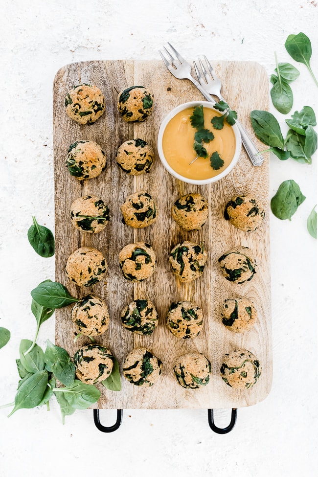 Spinach balls on a wooden cutting board with a side of mustard sauce.