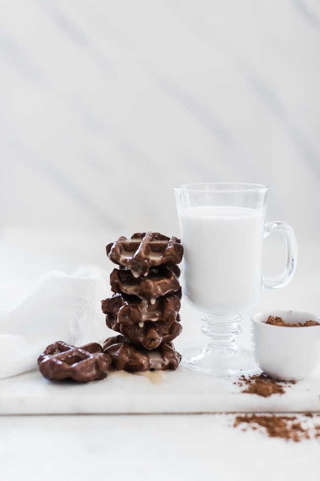 Chocolate waffle cookies stacked, next to a glass of milk.