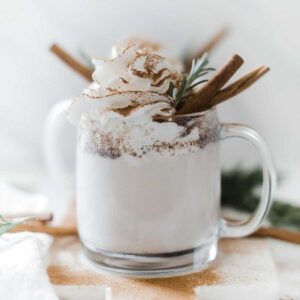 Pressure cooker warm milk and cinnamon in glass mugs, topped with whipped cream and garnished with rosemary and a cinnamon stick in a glass mug.
