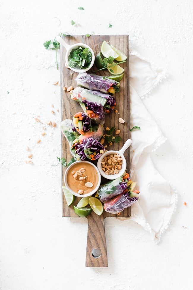 Easy spring roll recipe arranged on a wooden cutting board. Peanut dipping sauce and peanuts to the side.