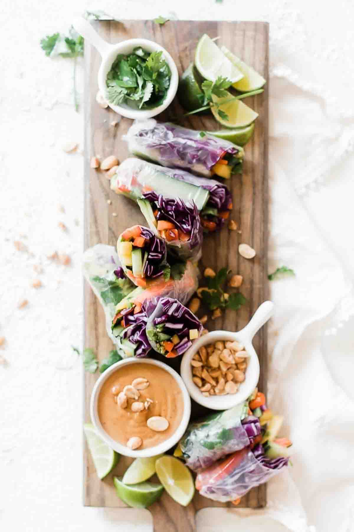 Easy spring roll recipe arranged on a wooden cutting board. Peanut dipping sauce and peanuts to the side.